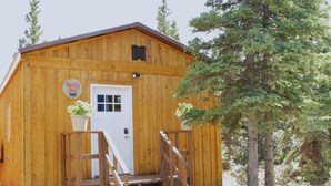 A wooden cabin with a white door, a small porch, and a staircase leading up to the entrance. - Arctic Dragonfly Inn (Healy)