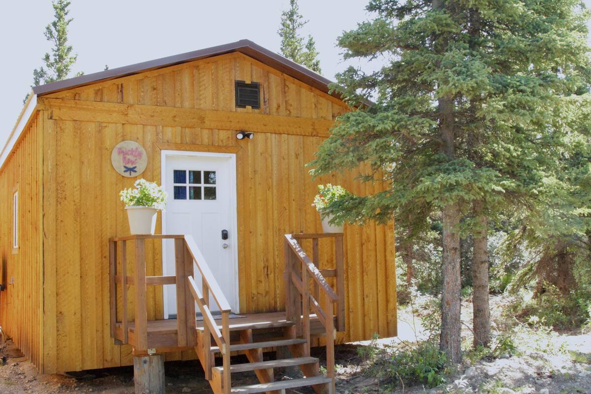 A wooden cabin with a white door, a small porch, and a staircase leading up to the entrance.
