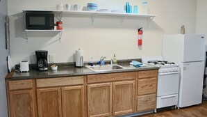 A kitchen with wooden cabinets, a microwave, a stove, a sink, and a refrigerator. - Arctic Dragonfly Inn (Healy)