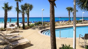 Un área junto a la piscina con sillones reclinables, una piscina, palmeras y vistas al océano y al muelle.
