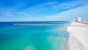Una playa con un muelle largo que se adentra en el océano, una orilla arenosa y un cielo azul despejado.