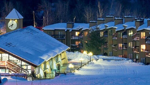 A snow-covered building with a clock tower, surrounded by other buildings with balconies. - Okemo Mountain Lodging  by Vail Resorts (Ludlow)