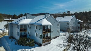 A large, light blue, multi-story house with a balcony on the second floor, surrounded by snow. - Okemo Mountain Lodging  by Vail Resorts (Ludlow)