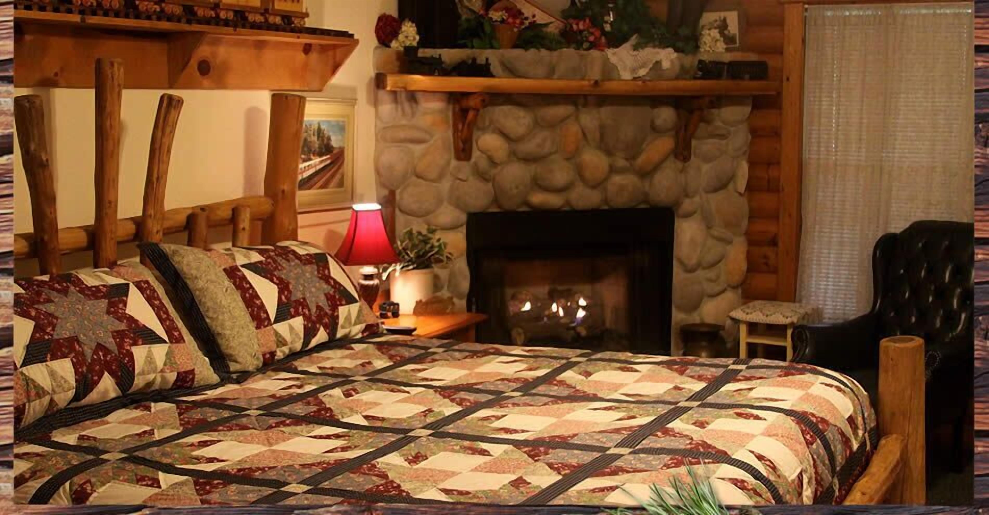 Una habitación acogedora con una cama grande, una chimenea, una silla de madera y una lámpara.