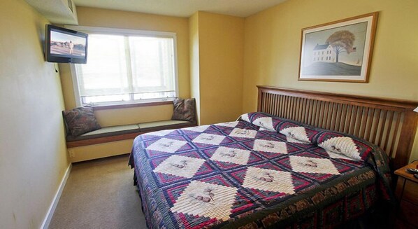 A bedroom with a large bed, a window seat, a television, and a framed picture on the wall. - Okemo Mountain Lodging by Vail Resorts (Ludlow)