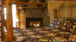A cozy bedroom with a stone fireplace, a wooden bed frame, and a quilted bedspread. - Okemo Mountain Lodging  by Vail Resorts (Ludlow)