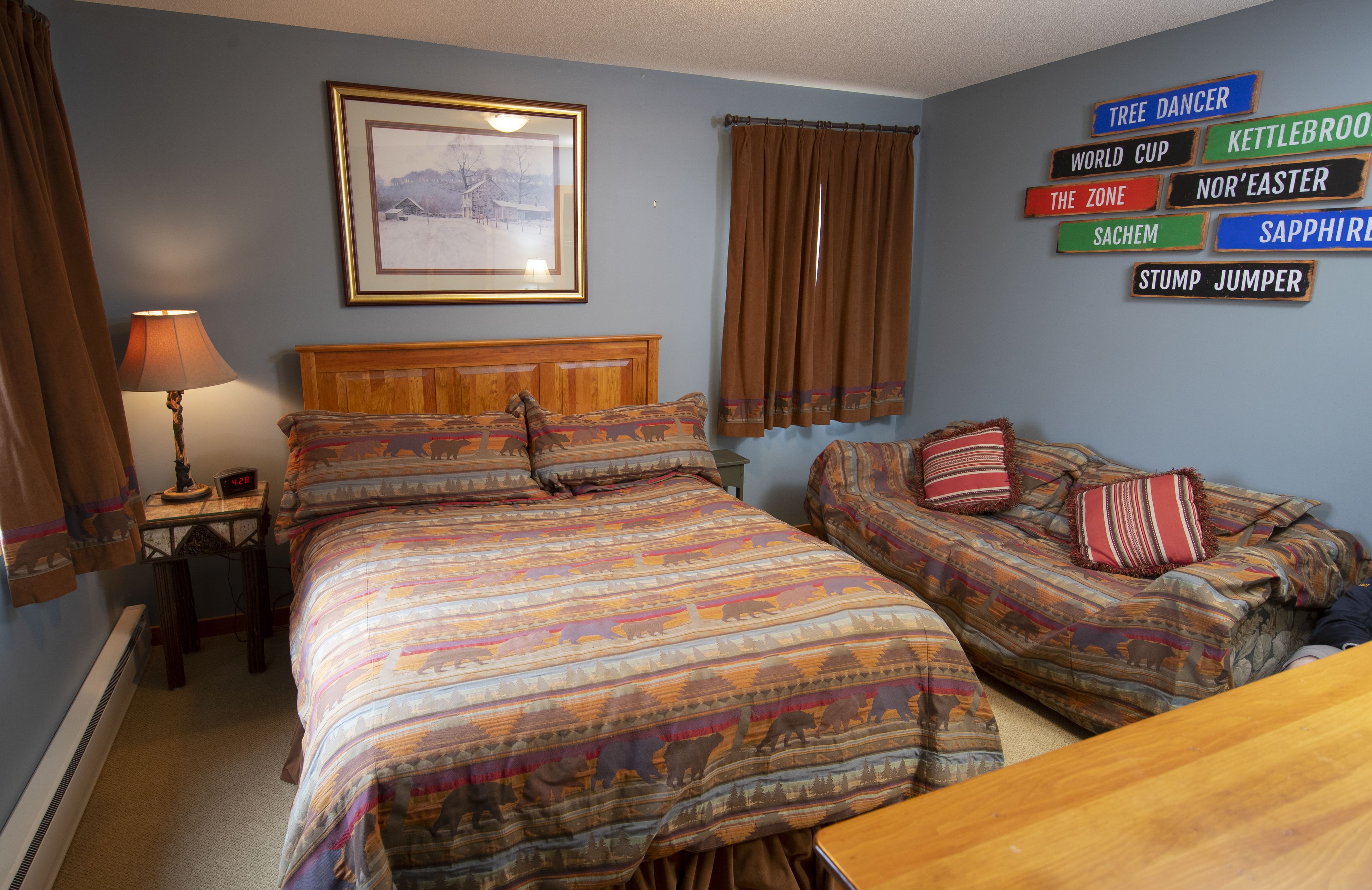 Une chambre avec deux lits, un tableau encadré au mur et une pancarte portant différents noms.