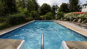 A swimming pool with a metal ladder, surrounded by a fence and lounge chairs. - Okemo Mountain Lodging  by Vail Resorts (Ludlow)