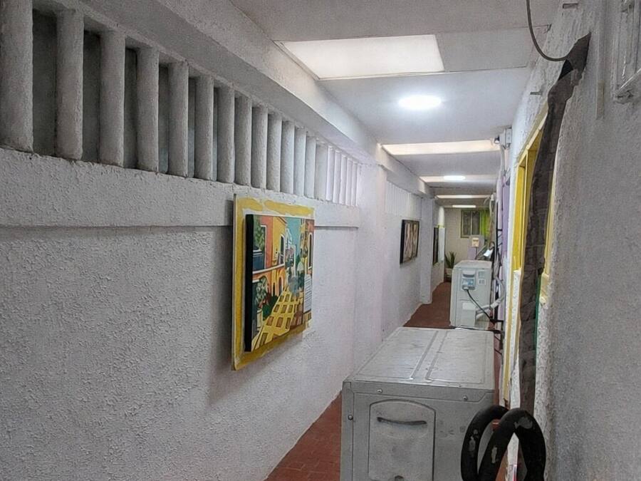 A hallway with a tiled floor, a row of trash bins, a large metal cabinet, and a colorful mural on the wall.