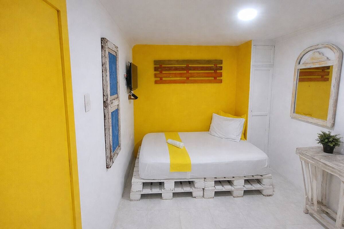 A room with a bed, a door, a wall-mounted shelf, and a mirror.