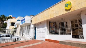 A building with a white facade, a blue sign reading 'GEOGRAFIA CASAPOS', and a yellow 'GuestHouse' sign. - Quillahost Guesthouse (Barranquilla)