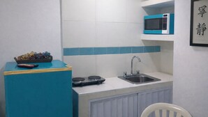 A compact kitchen with a sink, a microwave, a stove, and a chair.