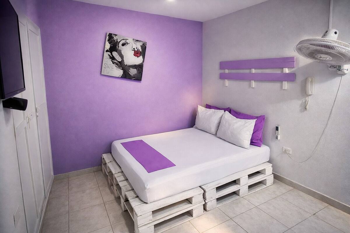 A bedroom with a bed on pallets, a purple wall, and a painting.