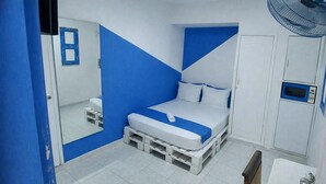 A bedroom with a bed, a mirror, a fan, and a microwave. - Quillahost Guesthouse (Barranquilla)