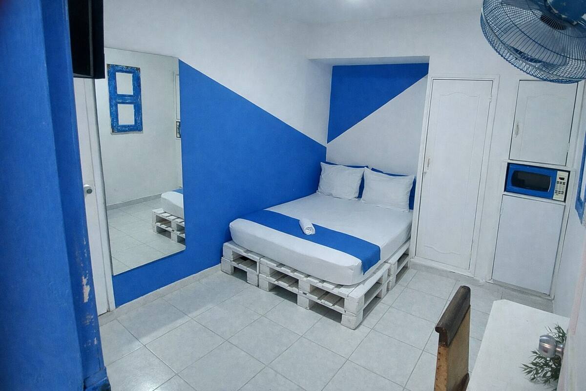 A bedroom with a bed, a mirror, a fan, and a microwave.