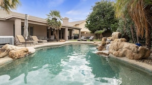 Ein Pool mit Steinen und Liegestühlen, umgeben von einem Haus und Palmen.
