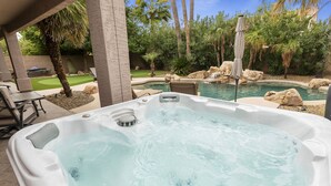 Ein Whirlpool mit Wasserfall, umgeben von einem angelegten Garten mit Palmen und einem Pool.