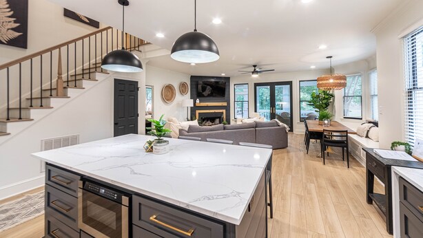 A modern kitchen with a marble island, wooden cabinets, and a built-in oven. There is a staircase with wooden railings leading to another level. - Pet friendly Reynolds Lake Oconee Retreat with Common Areas and Dock Access. (Greensboro)