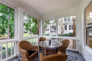 En inglasad veranda med möbler i rotting och ett bord i glas, med utsikt över ett bostadsområde.