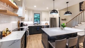 A modern kitchen with white cabinetry, a marble island, and a large window. - Pet friendly Reynolds Lake Oconee Retreat with Common Areas and Dock Access. (Greensboro)