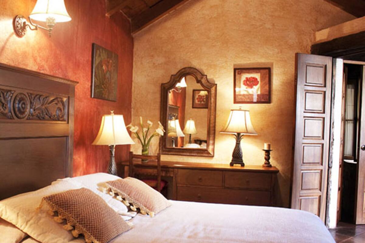 A bedroom with a large bed, two bedside lamps, a dresser, a mirror, and a door.