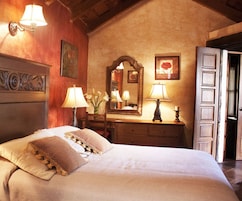 A bedroom with a large bed, two bedside lamps, a dresser, a mirror, and a door.