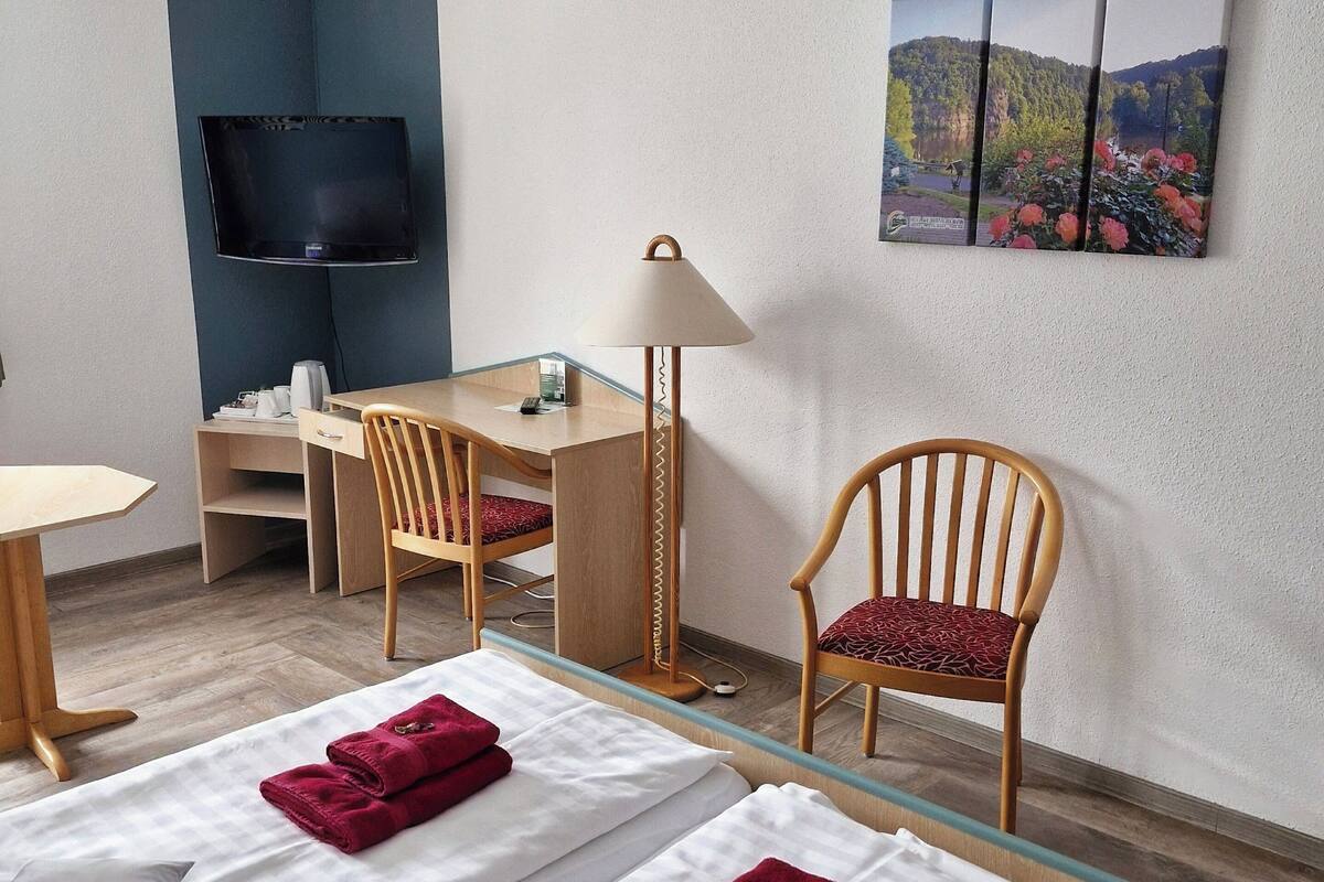 A hotel room with two beds, a desk, a chair, a TV, and a lamp.