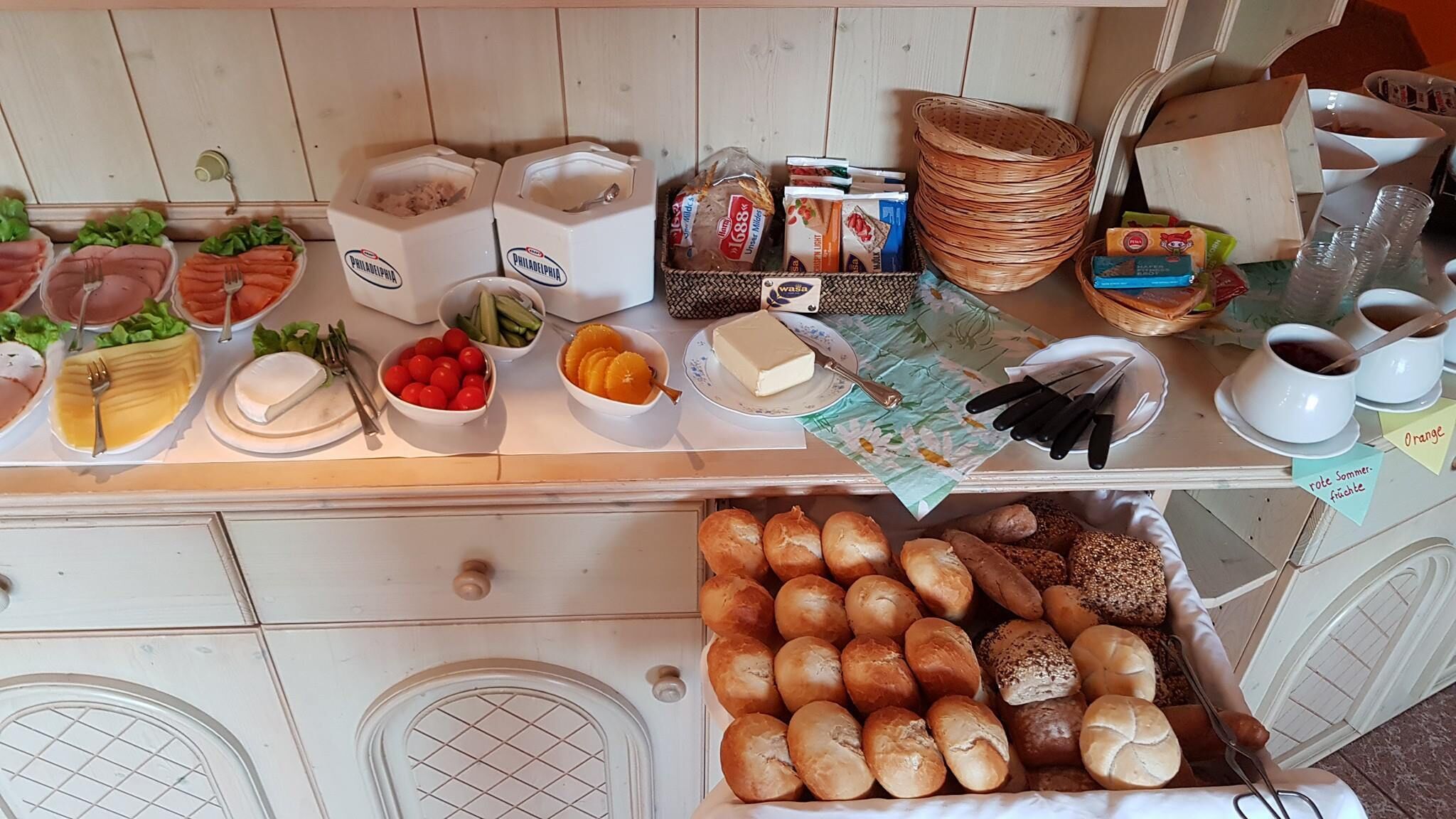 Une table de buffet proposant une variété d’aliments, notamment des viandes, des fromages, des fruits et des pains.