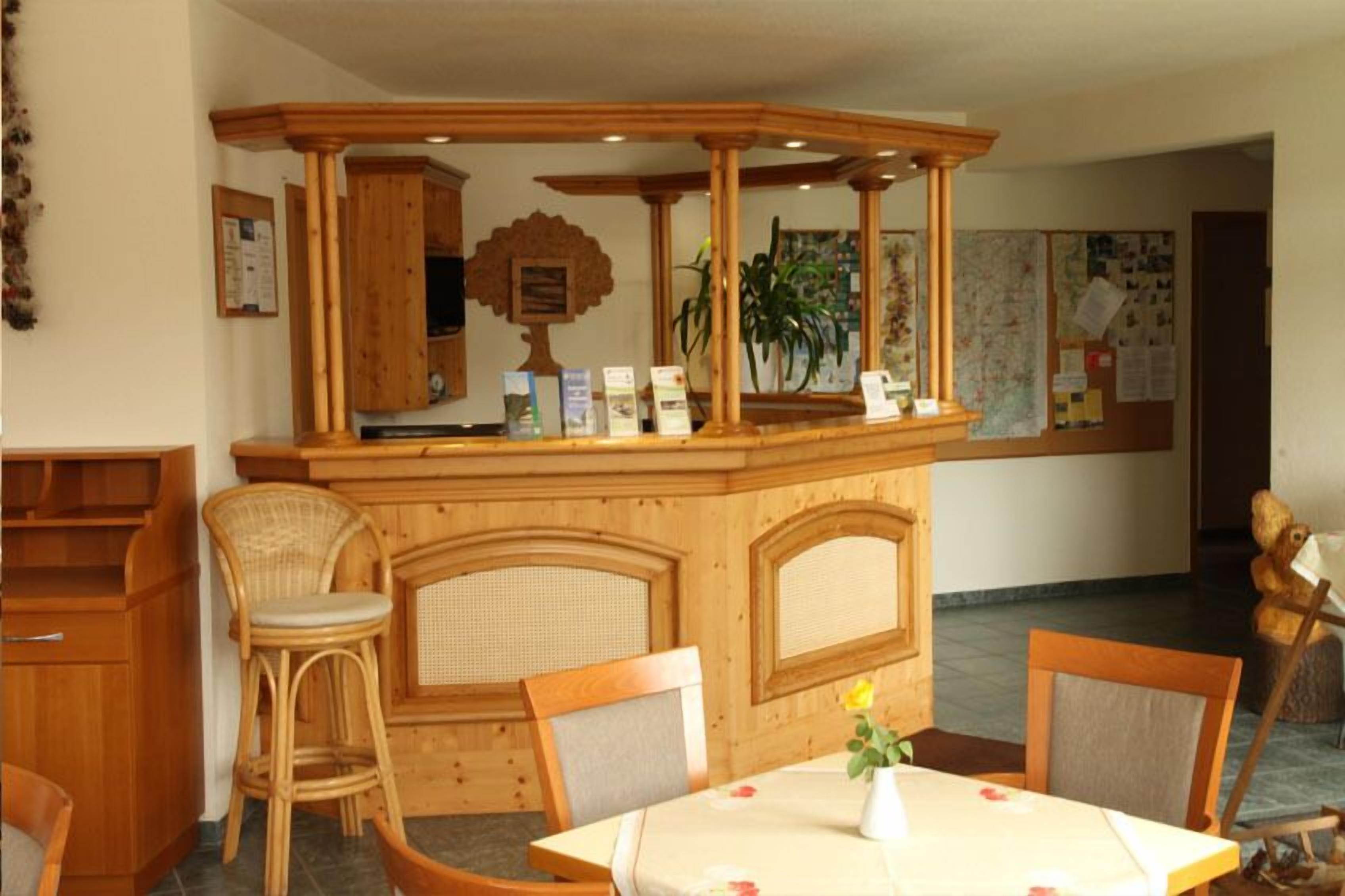 A wooden bar area with a counter, wicker chairs, and a table with a vase.