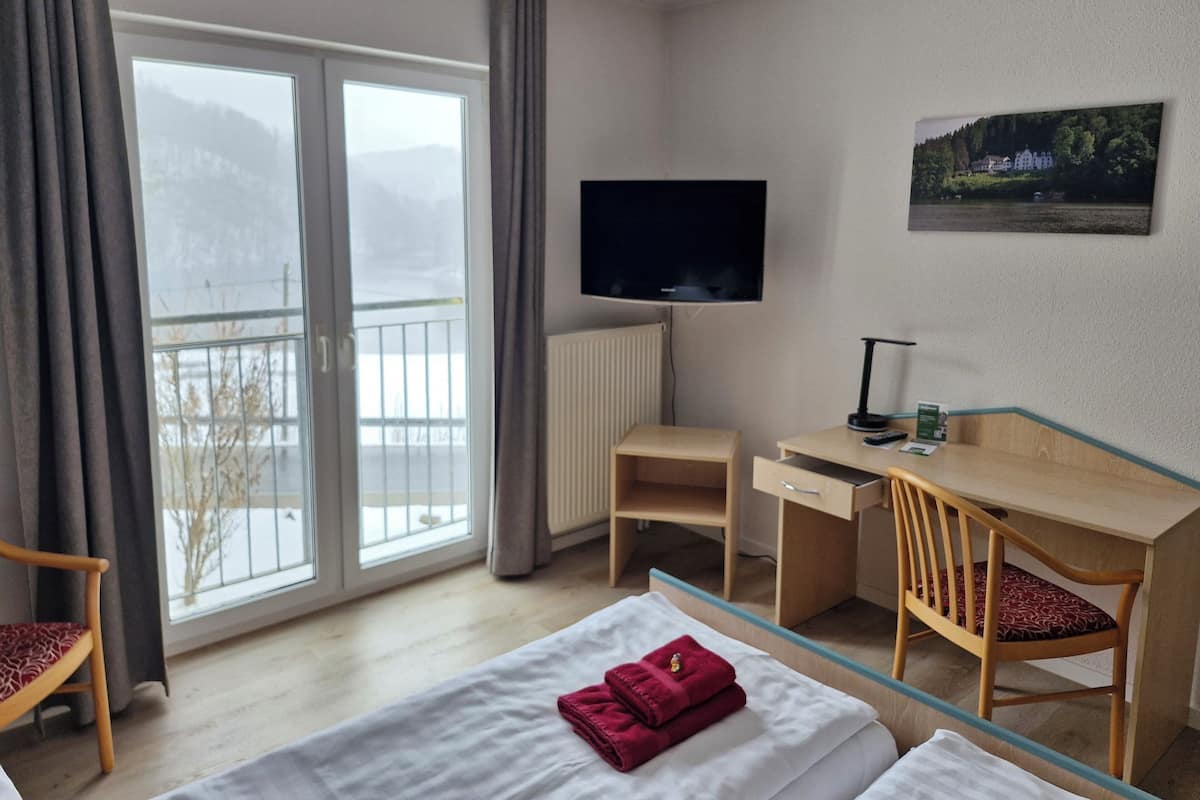 A hotel room with a bed, a desk, a chair, a TV, and a balcony with a view of the mountains.