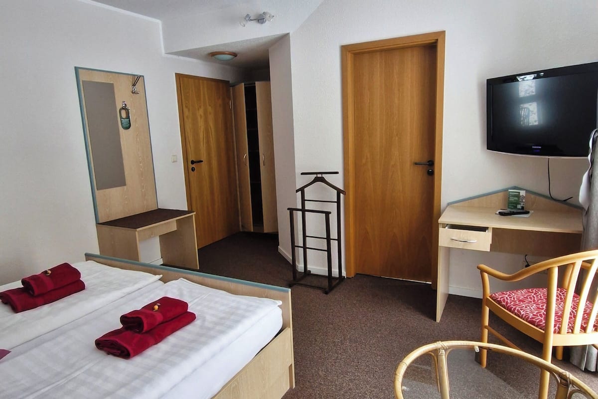 A hotel room with a bed, a desk, a chair, a television, and a wardrobe.