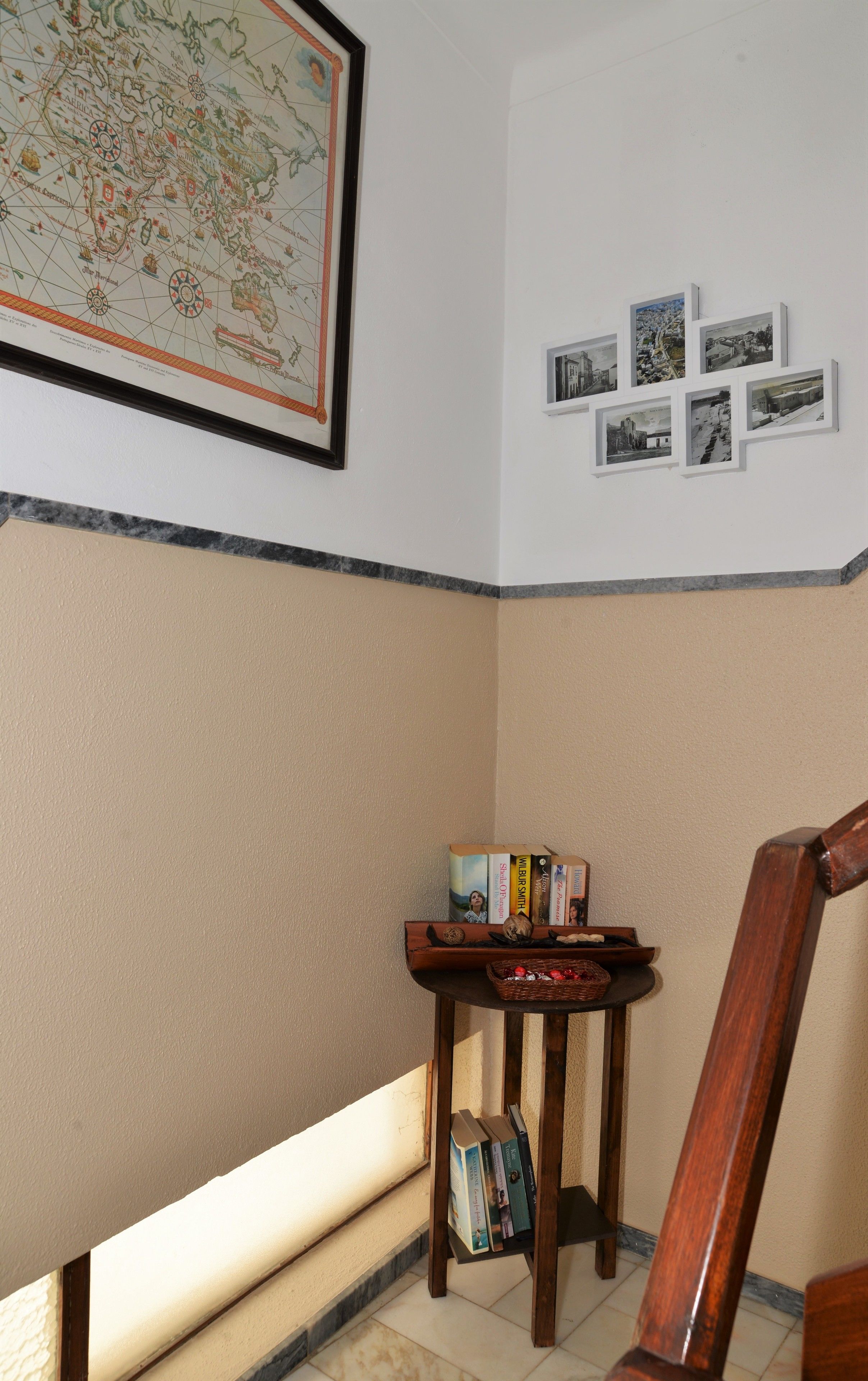 Un coin de pièce avec une carte encadrée accrochée au mur, une petite table sur laquelle sont posés des livres et des objets décoratifs, et une chaise en bois.