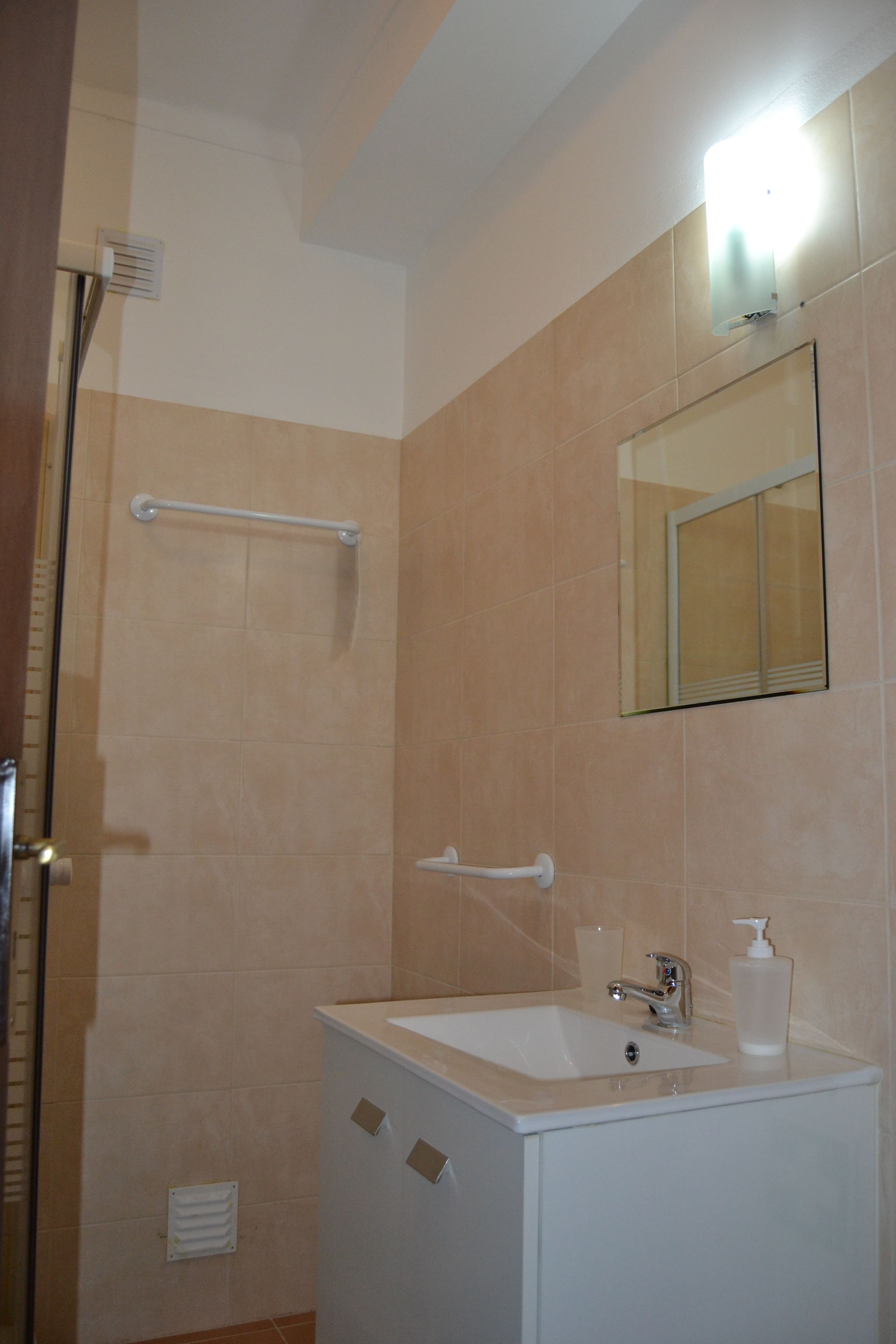 Un bany amb un lavabo blanc, un mirall i una zona de dutxa.