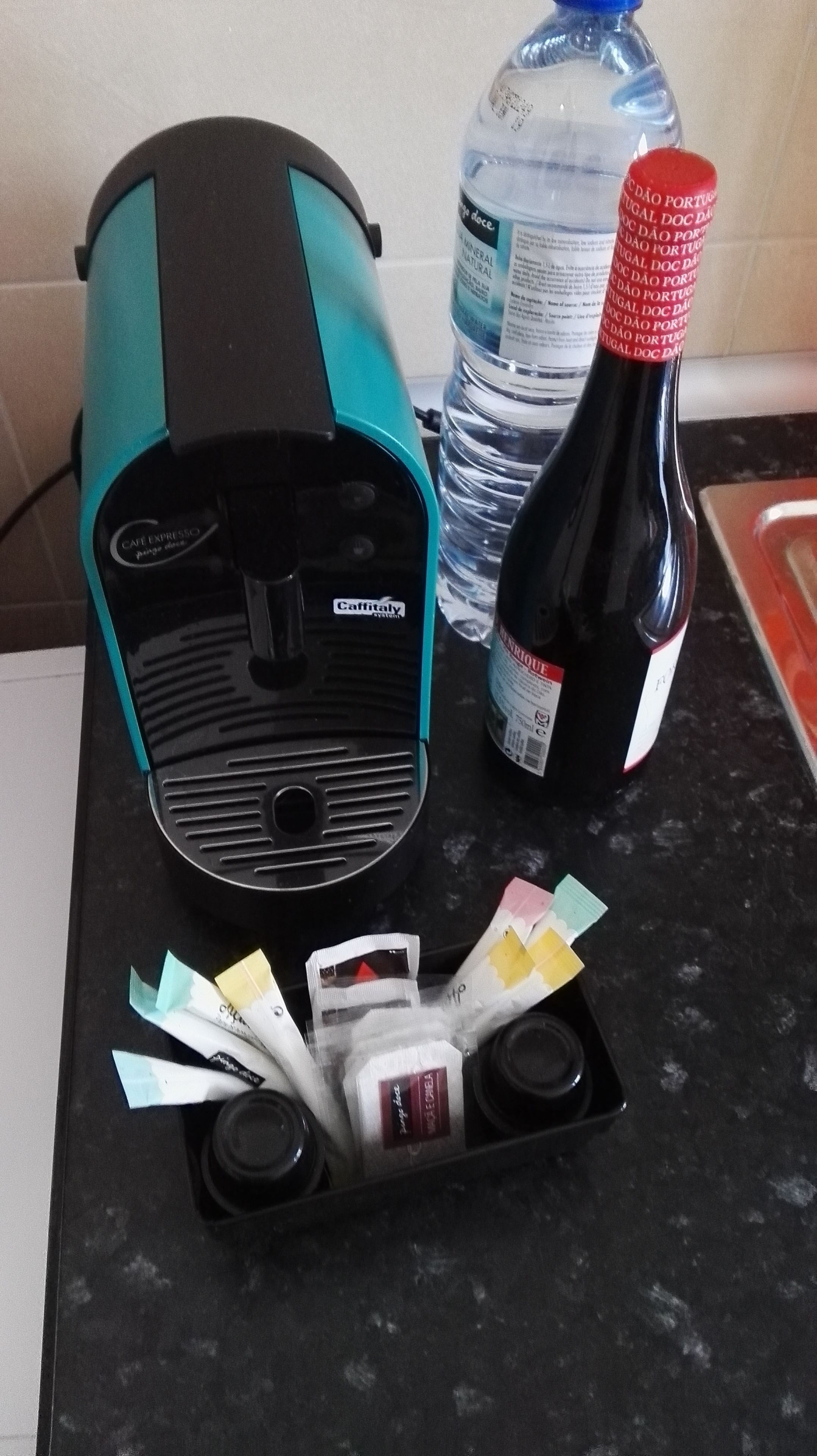 Eine Küchenarbeitsplatte mit Kaffeemaschine, einer Wasserflasche, einer Weinflasche und Kaffeeweißer-Portionen.