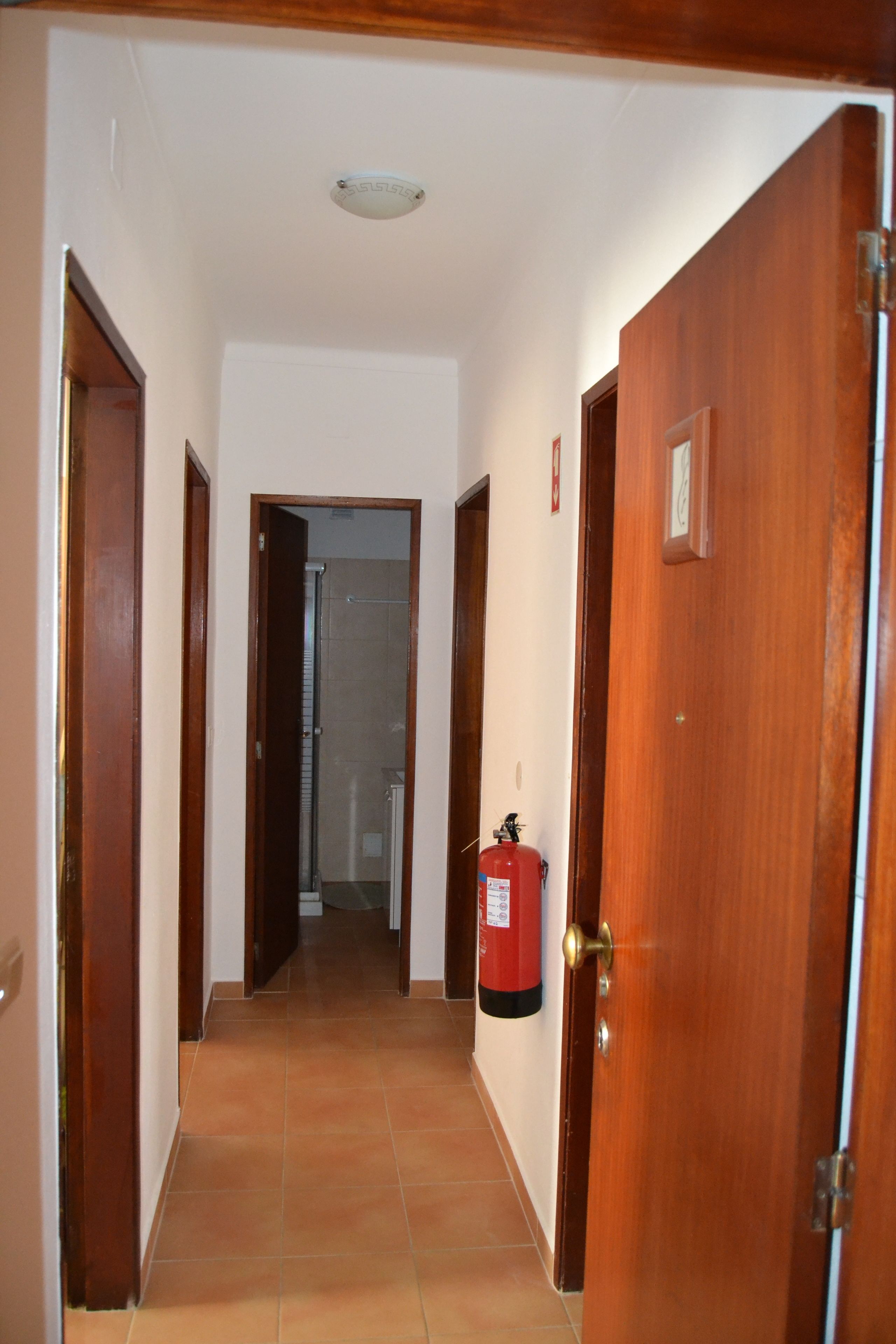 A hallway with wooden doors, a fire extinguisher mounted on the wall, and a tiled floor.