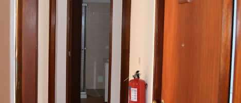 A hallway with wooden doors, a fire extinguisher mounted on the wall, and a tiled floor.