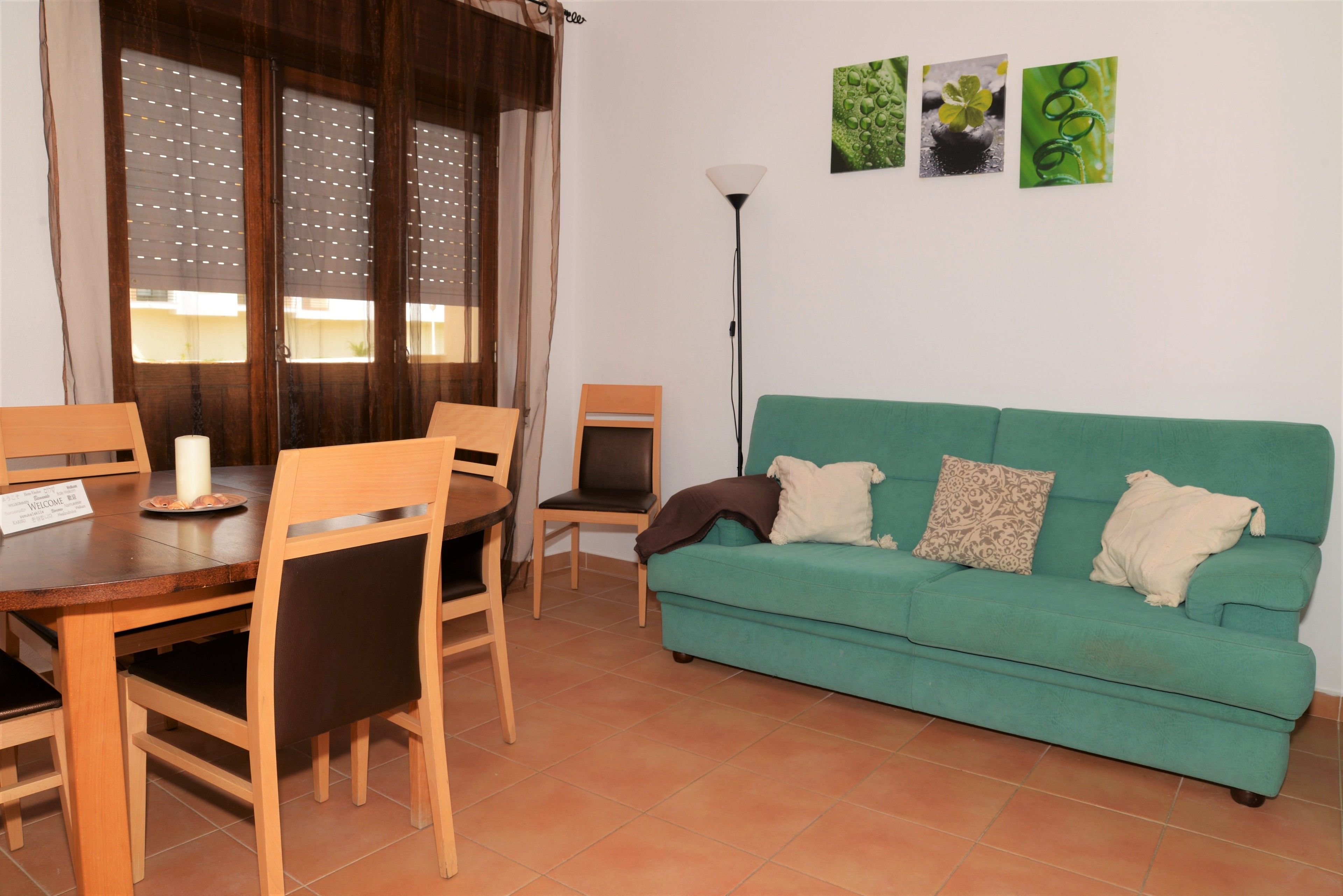 A dining area with a wooden table and chairs, a green sofa, and a floor lamp.