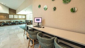 A modern hotel lobby with a long reception desk, several bar stools, a seating area with couches and chairs, and a wall decorated with leaf-shaped mirrors. - Holiday Inn Historic (St. Augustine)