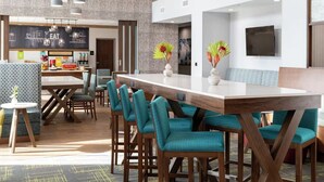 A modern dining area with a long wooden table, teal upholstered chairs, and pendant lighting. - Holiday Inn Historic (St. Augustine)