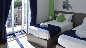 A hotel room with two beds, a green accent wall, a decorative piece above the beds, and a view through a glass door. - Specchio di Parthenope (Naples)