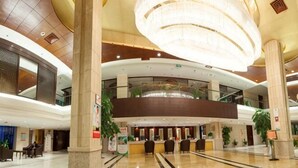 A spacious lobby with a reception desk, large columns, and a high ceiling with a chandelier.