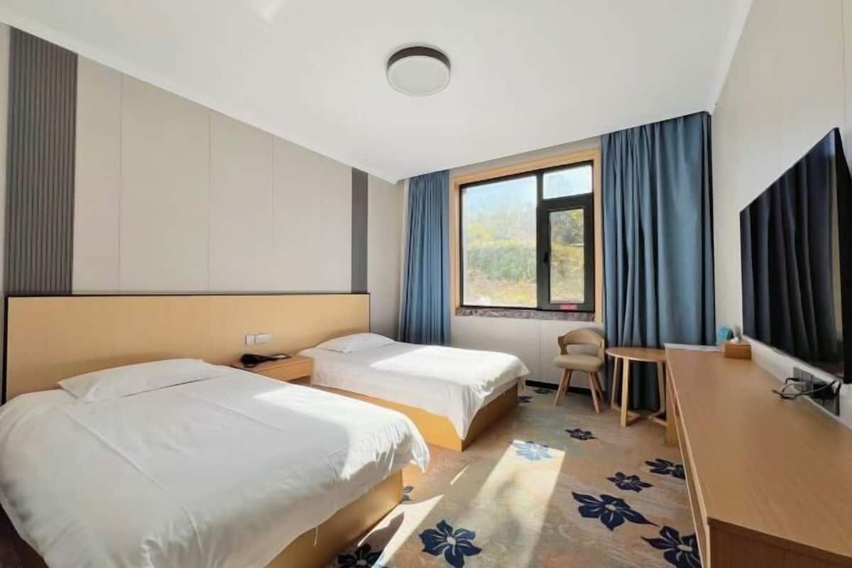 Une chambre d’hôtel avec deux lits, un bureau, une chaise, une télévision et une fenêtre avec des rideaux.