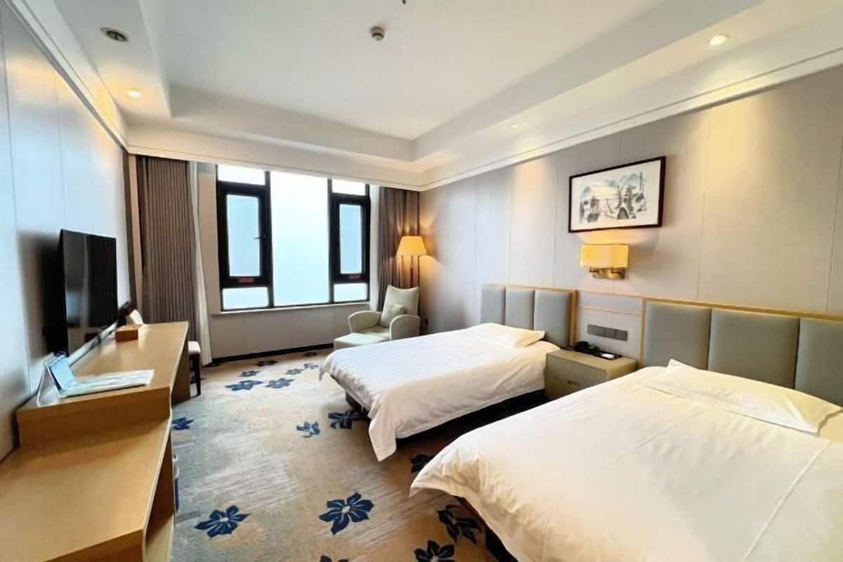 Une chambre d’hôtel avec deux lits, un bureau, une chaise, une télévision et une fenêtre.