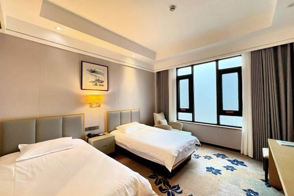 Une chambre d’hôtel avec deux lits, un bureau, une chaise, une fenêtre avec des rideaux et une lampe fixée au mur.
