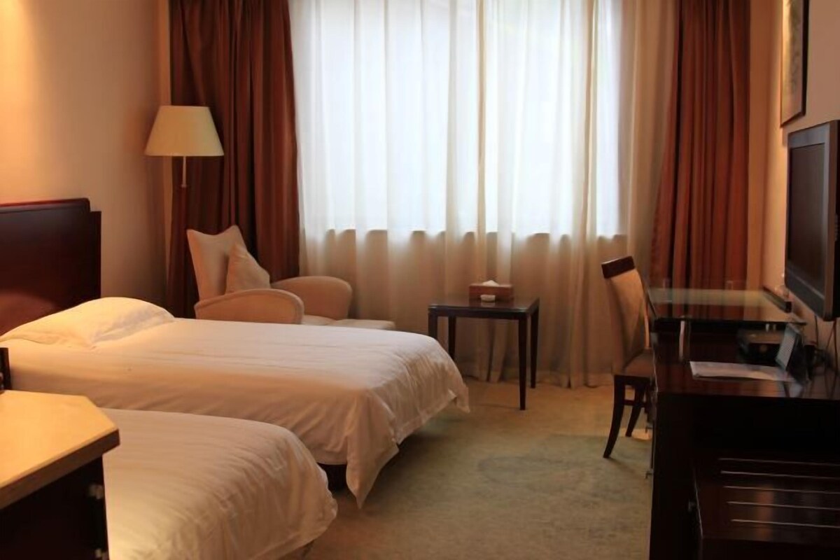 Une chambre d’hôtel avec deux lits, un bureau, une chaise, une télévision et une lampe.