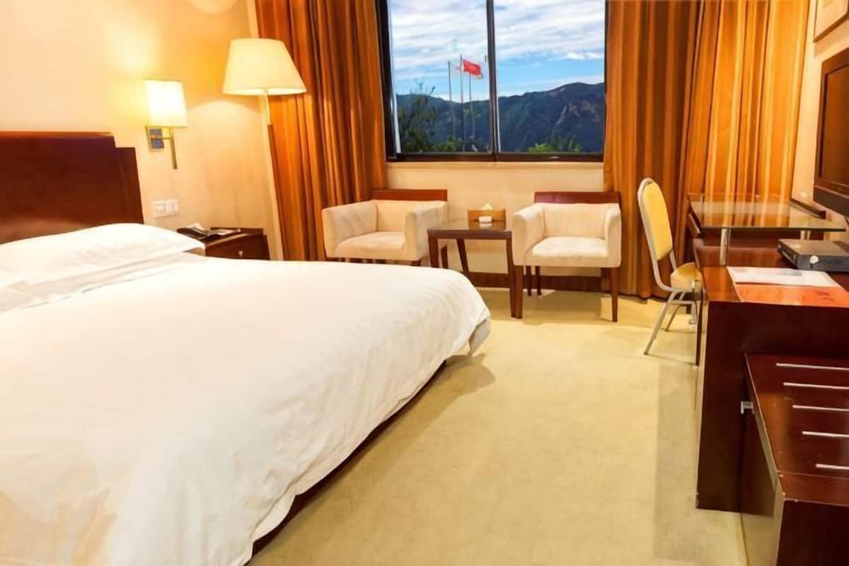 Une chambre d’hôtel comprenant un lit, un bureau, deux chaises, une petite table et une fenêtre avec des rideaux.