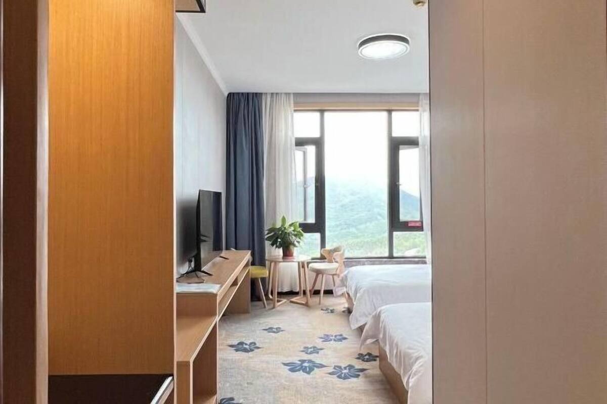 Une chambre d’hôtel avec un lit, un bureau et une chaise, une télévision et une fenêtre avec des rideaux.