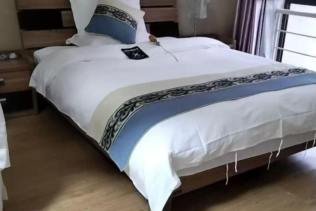 Una cama bien tendida con una colcha blanca y azul, un cabecero de madera y una mesita de noche con una lámpara.