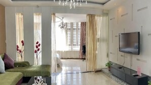 A modern living room with a sofa, a flat-screen TV, a chandelier, and a view into another room. - Li'ao Apartment Hotel (NANTONG)