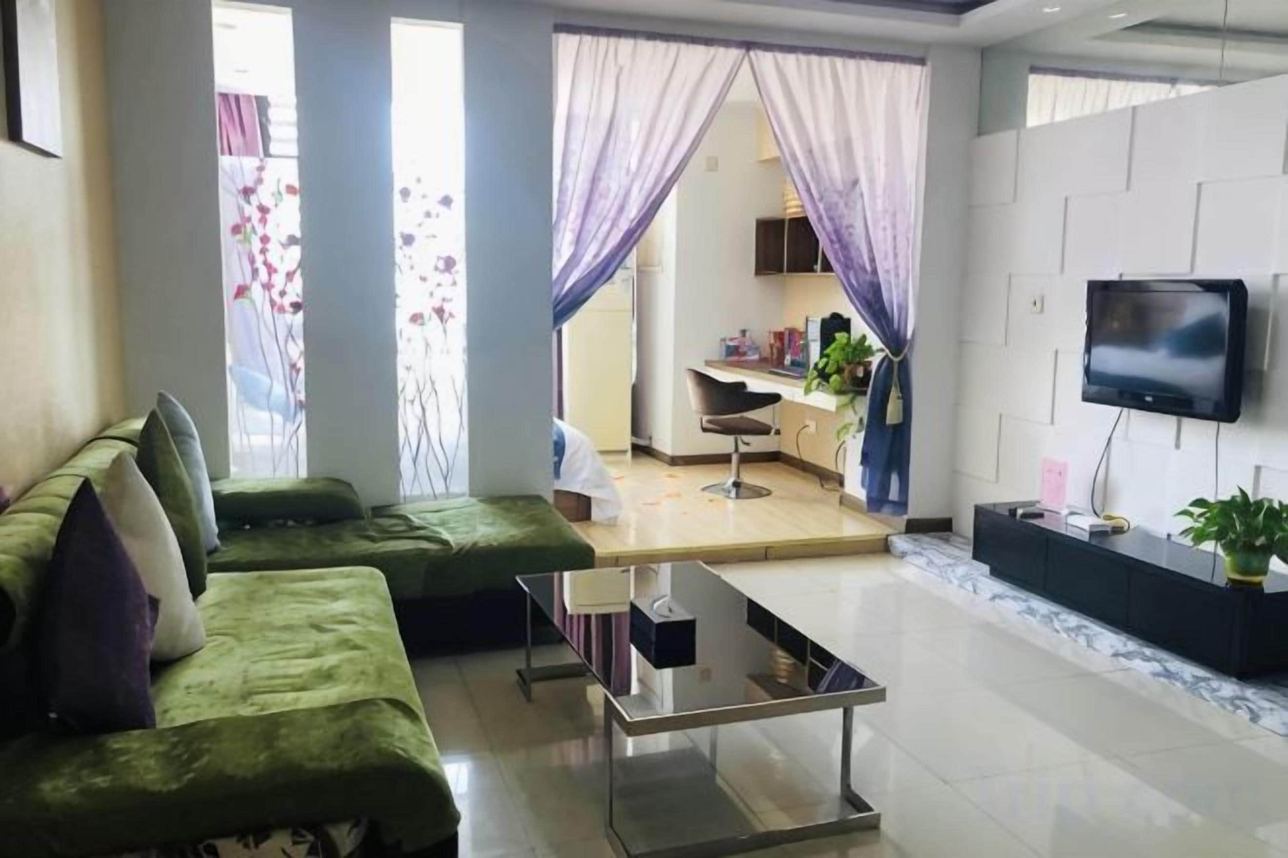 A modern living room with a green sofa, a coffee table, and a flat-screen TV mounted on the wall.